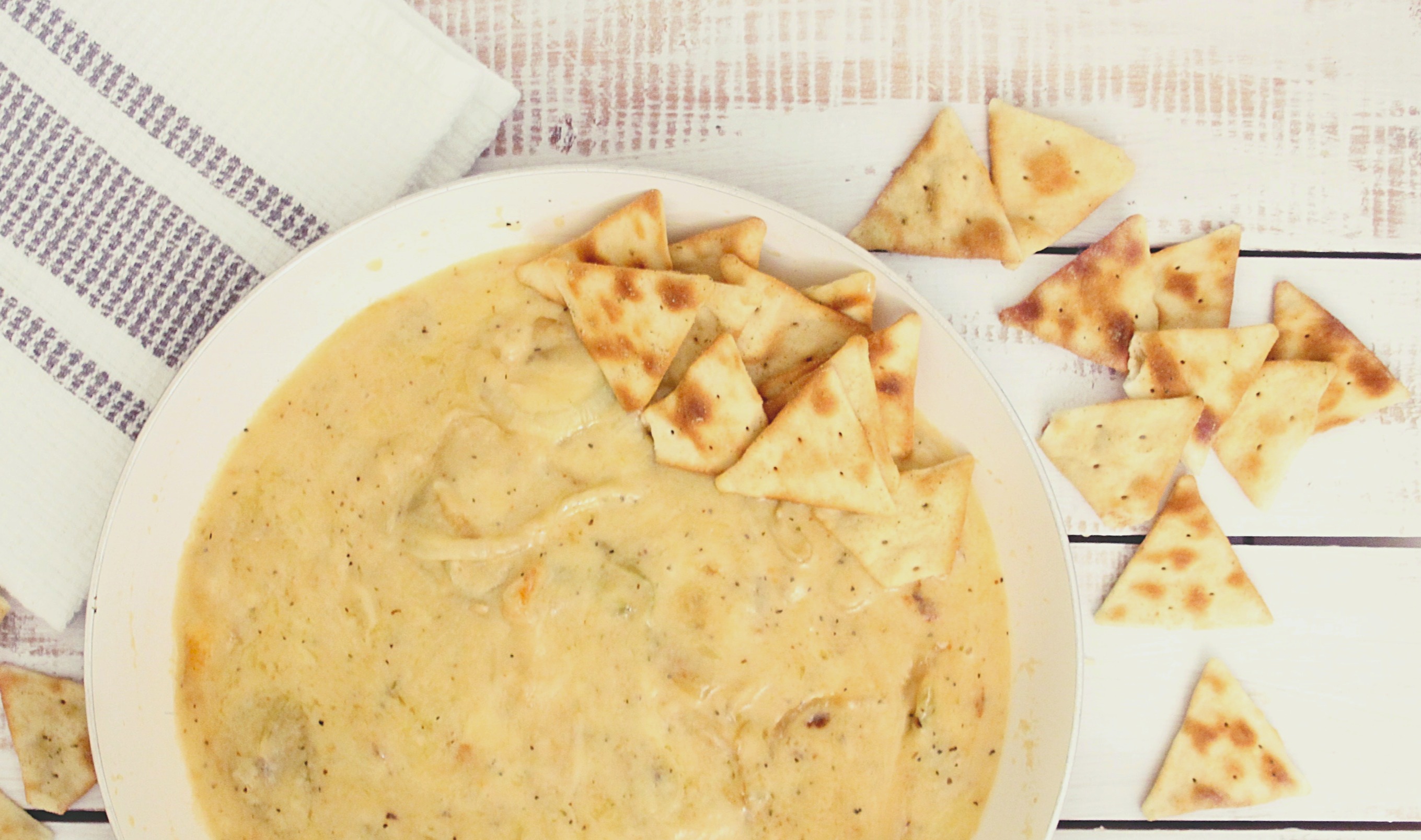 white chili in bowl on striped tablecloth with triangle shaped crackers